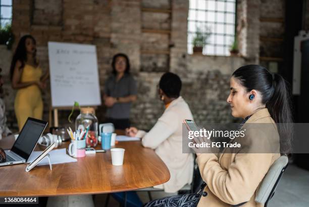 visually impaired businesswoman using smartphone and earphones during business meeting - accessibility blind stock pictures, royalty-free photos & images