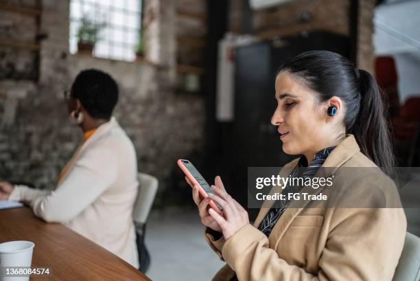 visually impaired businesswoman using smartphone and earphones during business meeting - blindness imagens e fotografias de stock