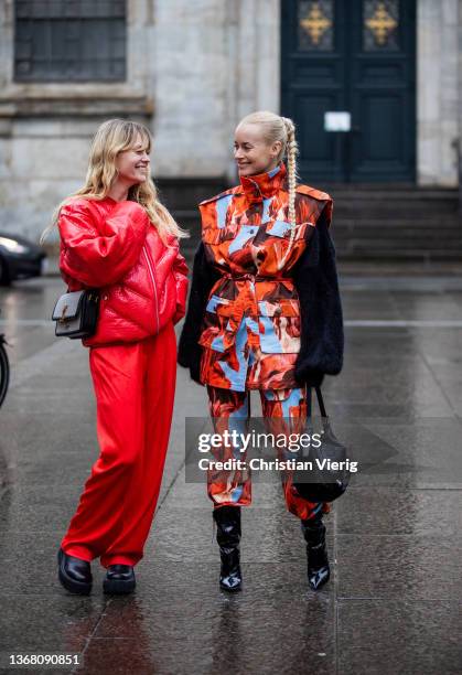 Thora Valdimars wearing camouflage belted jacket and pants, ankle boots & Jeanette Friis Madsen wearing red jacket, pants seen outside Lovechild 1979...