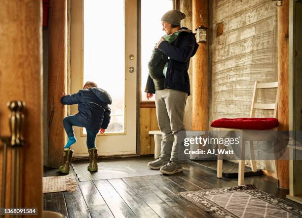 boy putting on shoe with mother standing by at front door of eco cabin - sneeuwschoen stockfoto's en -beelden