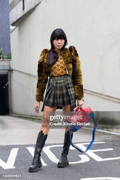 Susie Lau wears a Richard Malone jacket, Ganni boots, velvet printed top, kilt mini skirt and a Mulberry x Richard Malone bag during London Fashion...