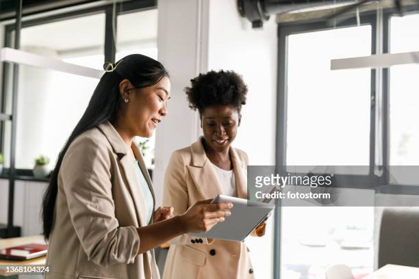 zwei geschäftsfrauen, die während eines meetings daten auf einem digitalen tablet betrachten - diverse business people stock-fotos und bilder