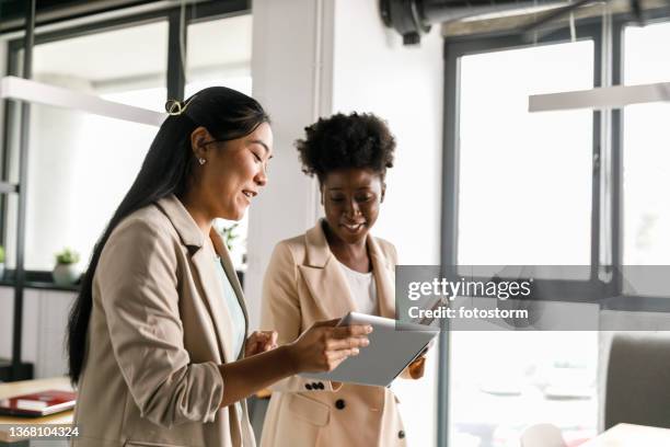 two businesswomen looking at data on digital tablet while going on a meeting - returning computer stock pictures, royalty-free photos & images