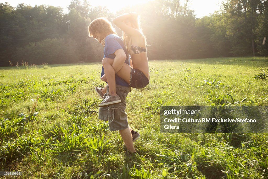 Man carrying girlfriend in rural field