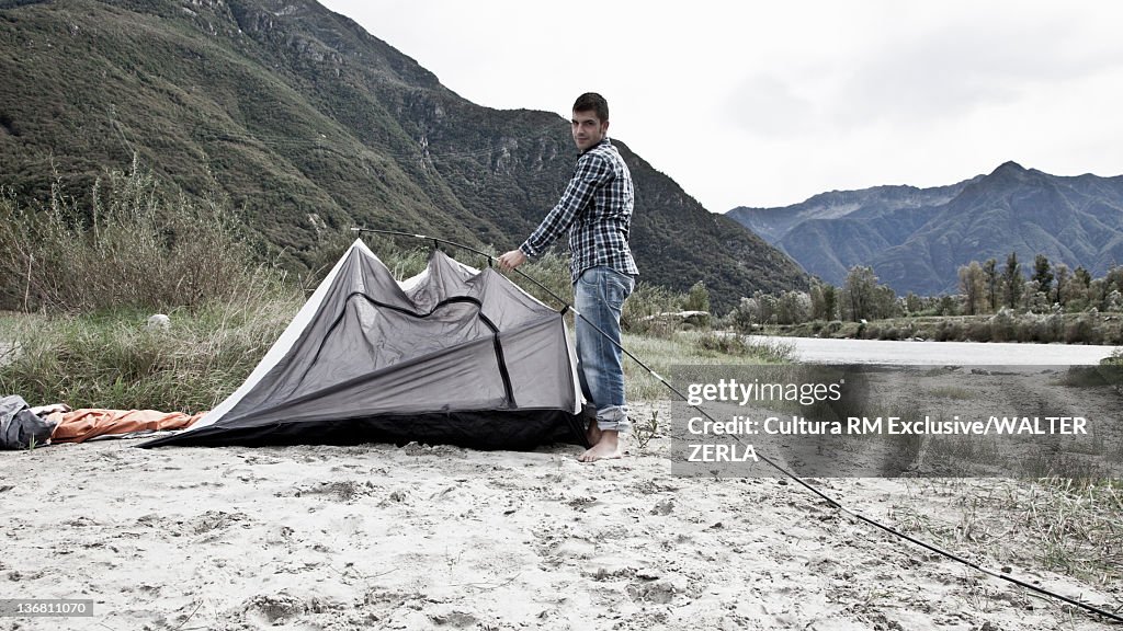 Man pitching a tent by lake