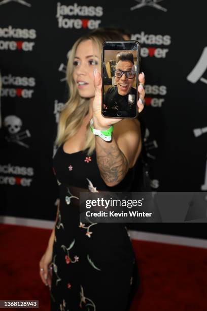 Lux Wright, Steve-O's fiancée, displays a mobile phone showing Steve-O on FaceTime as she attends the U.S. Premiere of "Jackass Forever" at TCL...