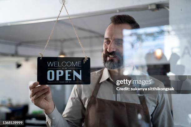 barista hanging up an open sign on the window of him coffee shop. - open sign stock pictures, royalty-free photos & images