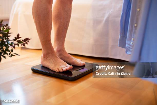 senior man standing on weight scale, low section - weegschaal stockfoto's en -beelden