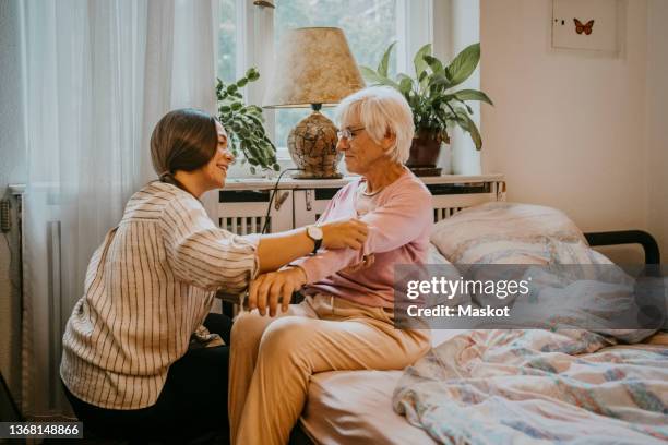 female healthcare worker helping senior woman to wear sweater in bedroom - home caregiver stock pictures, royalty-free photos & images