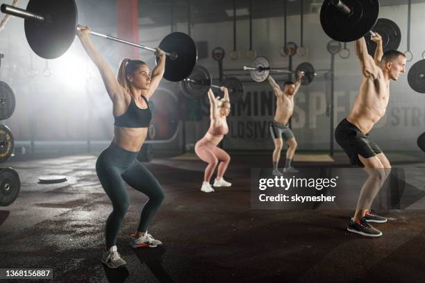 group of athletic people exercising with barbells during cross training in a gym. - snatch weightlifting stock pictures, royalty-free photos & images