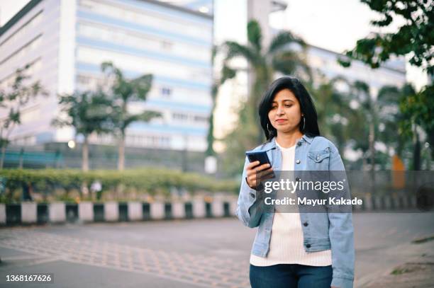 woman standing on a city street and using her mobile phone in business area - india phone professional stock pictures, royalty-free photos & images