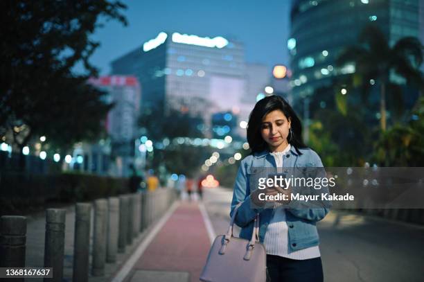 woman standing on a city street and using her mobile phone in business area - india phone professional stock pictures, royalty-free photos & images