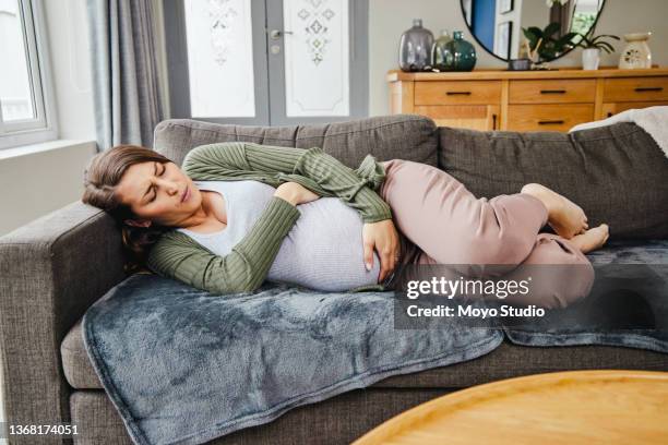 shot of a young expecting mother experiencing contractions at home - morning sickness stockfoto's en -beelden