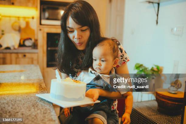 il viso e il corpo di un bambino sono coperti dai resti della sua torta di compleanno durante la sua prima festa di compleanno - parents children blow candles asians foto e immagini stock
