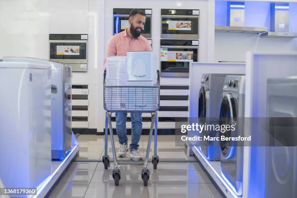 a young man looking at washing machines in an appliance store. - appliance shopping stock pictures, royalty-free photos & images