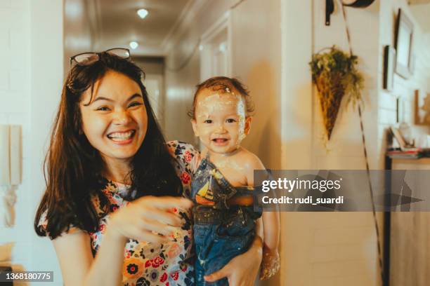 il viso e il corpo di un bambino sono coperti dai resti della sua torta di compleanno durante la sua prima festa di compleanno - parents children blow candles asians foto e immagini stock