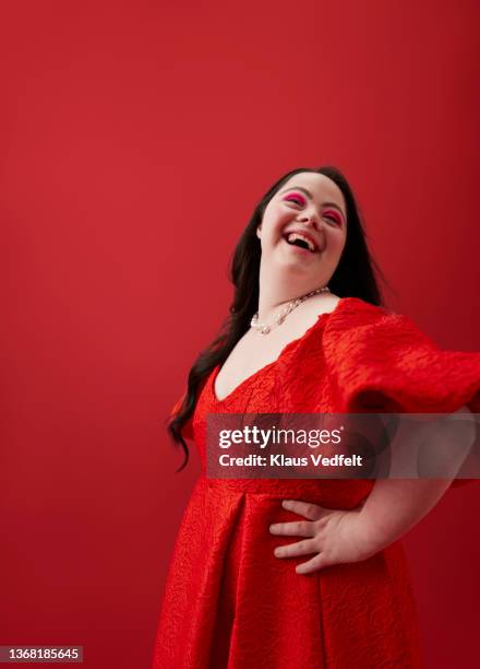 young woman with hand on hip against red background - portrait femme fond rouge adulte photos et images de collection