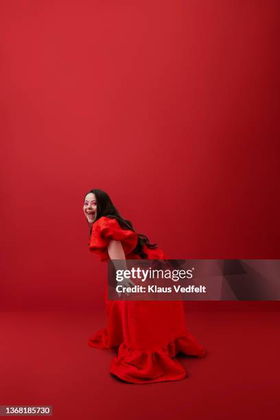 happy woman bending on knees against red background - woman fashion long dress stock pictures, royalty-free photos & images