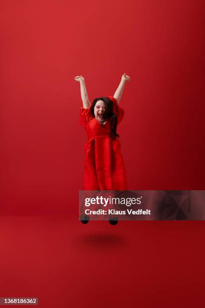 young woman jumping against red background - long dress stock pictures, royalty-free photos & images