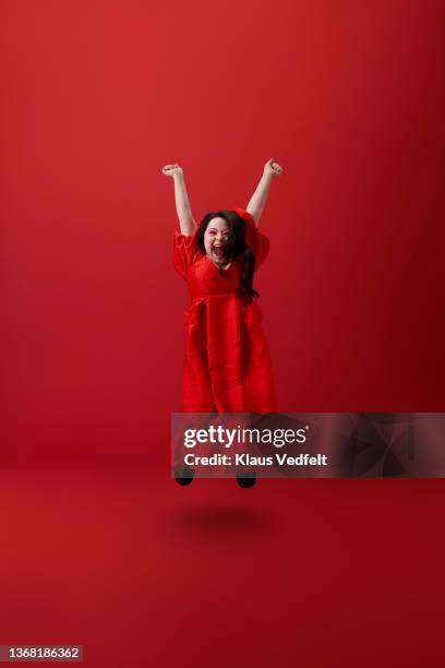 young woman jumping against red background - women in long dress stock pictures, royalty-free photos & images