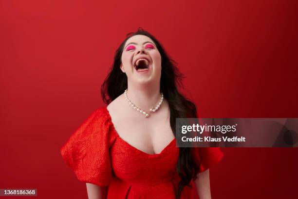 young woman laughing against red background - bright makeup stock pictures, royalty-free photos & images