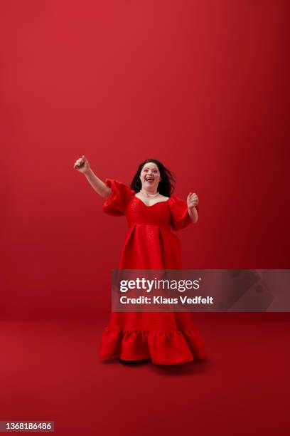happy woman with hand raised against red background - woman fashion long dress stock pictures, royalty-free photos & images