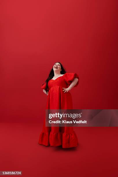 cheerful woman with hand on hip against red background - women in long dress stock pictures, royalty-free photos & images