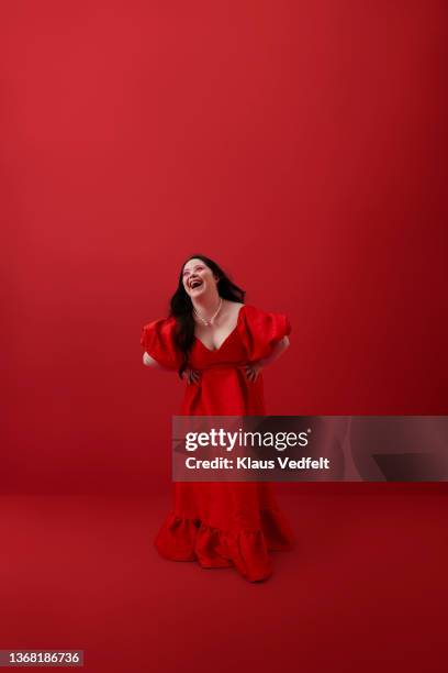 young woman laughing with hand on hip against red background - woman fashion long dress stock pictures, royalty-free photos & images