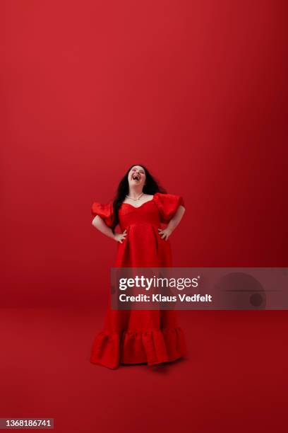 cheerful woman with hands on hip against red background - woman fashion long dress stock pictures, royalty-free photos & images