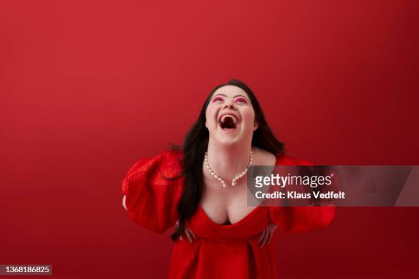 happy woman in red dress laughing against red background - female décolletage stock pictures, royalty-free photos & images