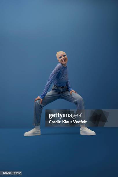 happy albino woman squatting against blue background - portrait blue background stock-fotos und bilder