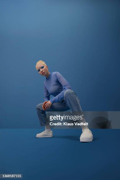 albino woman squatting against blue background - physical stance stock pictures, royalty-free photos & images