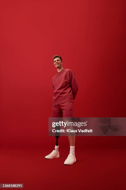 happy man standing with hands behind back - rode korte broek stockfoto's en -beelden