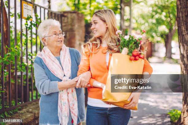 lächelnde enkelin kauft für ihre großmutter ein - eine helfende hand stock-fotos und bilder