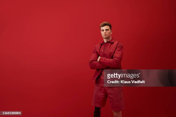 handsome man standing with arms crossed - red shirt stock-fotos und bilder
