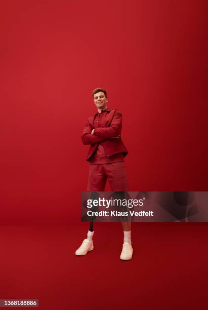 smiling man standing with arms crossed - rood jak stockfoto's en -beelden