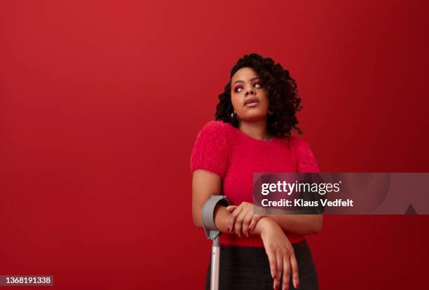 young woman with crutch looking away - portrait femme fond rouge adulte photos et images de collection