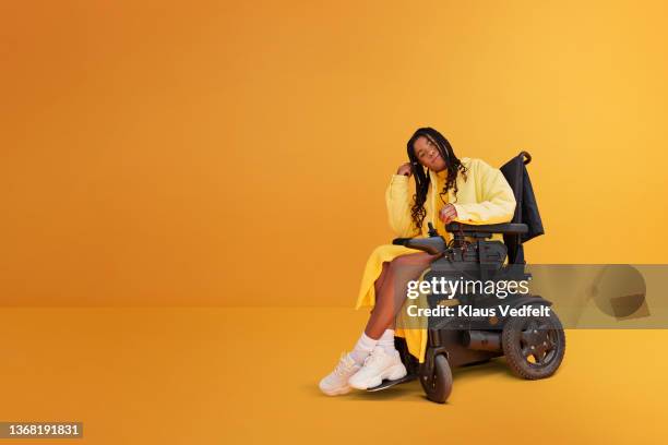 woman with disability in wheelchair against yellow background - hoofd schuin stockfoto's en -beelden