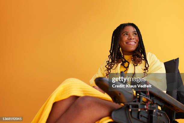 smiling woman looking away while sitting on wheelchair - frau rollstuhl selbstständigkeit stock-fotos und bilder