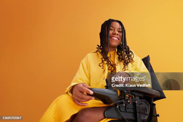 smiling woman on wheelchair against yellow background - woman wheelchair stock pictures, royalty-free photos & images
