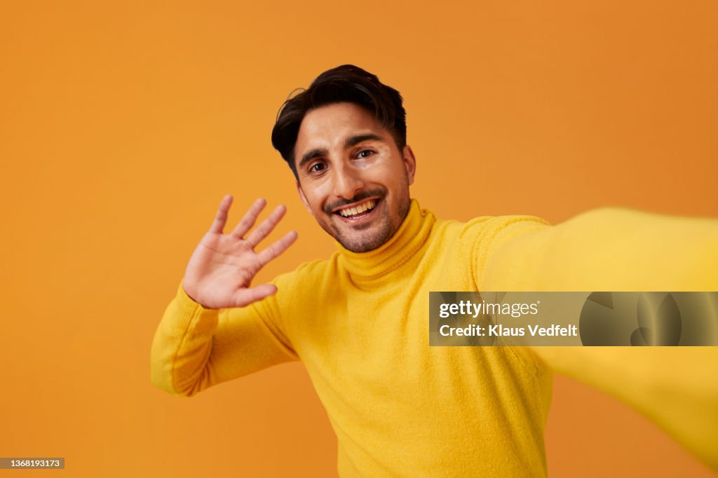 Happy man with vitiligo waving hand against yellow background