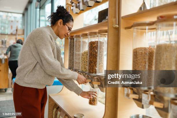 female using a nuts dispenser in a zero waste store - duurzaam consumeren stockfoto's en -beelden