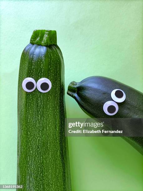 two funny zucchini with cartoon eyes on green background - wackelaugen stock-fotos und bilder