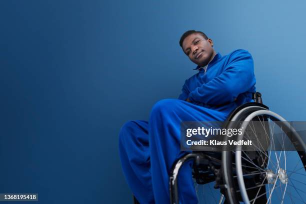 man with disability sitting with arms crossed in wheelchair - colour background cool portrait photography stockfoto's en -beelden