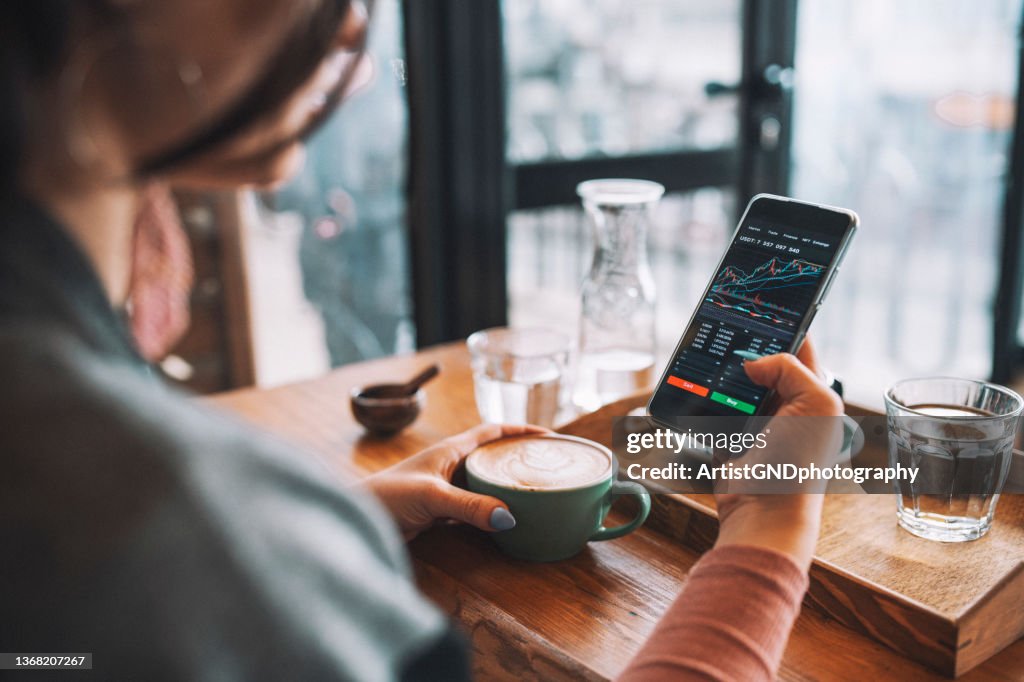 Frauen mit Smartphone kaufen Kryptowährung in einem Café, Blockchain-Investition, Dezentralisierung und Börsenkonzept.