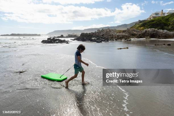 south africa, hermanus, boy (8-9) with surfboard on beach - com os pés na água imagens e fotografias de stock