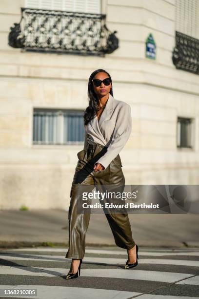 Emilie Joseph @in_fashionwetrust wears black sunglasses, silver earrings, a gold thick chain necklace from Merbabe, a beige oversized pinstriped...