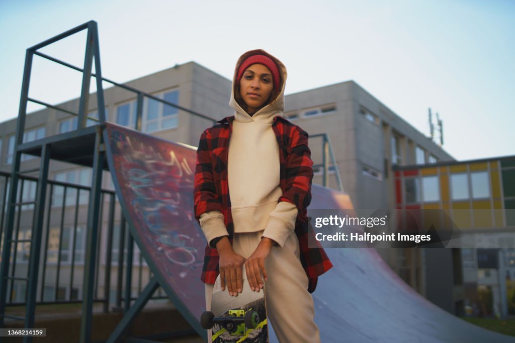 Young modern woman outdoors in the city, with skateboard, looking at camera.