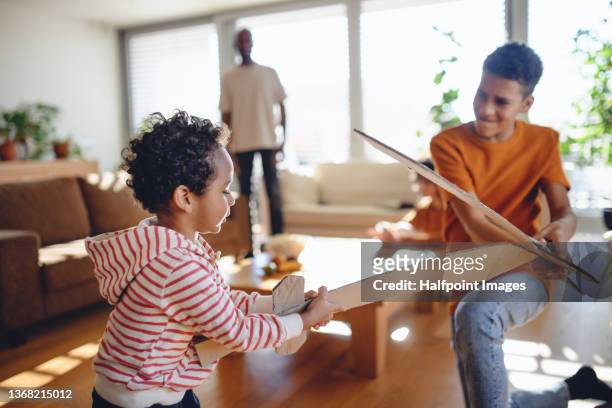 two happy multiracial brothers playing with cardboard swords at home. - brother fight stock pictures, royalty-free photos & images