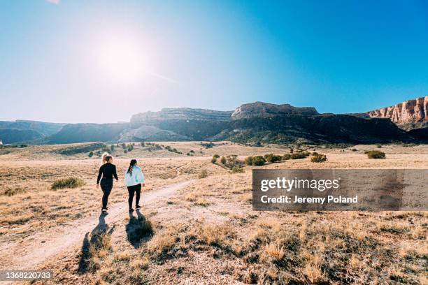 wide angle shot of two young women outdoors getting some exercise together in a desert recreational area on a hiking trail footpath near the colorado national monument in grand junction - following path stock pictures, royalty-free photos & images